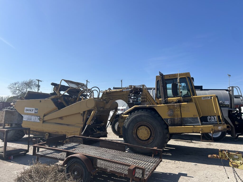 Yellow Caterpillar equipment parked on a lot, showcasing a Holt 613C Loader and attached trailer against a clear blue sky.